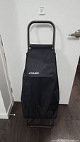 Front view of the Rolser black shopping trolley, showing flap with logo and solid structure.