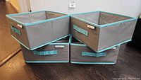 Four grey and turquoise foldable storage bins arranged stacked and side-by-side showing their size and handles on all sides.