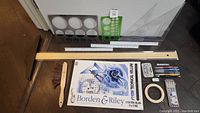 Top-down photo showing full lot: wooden T-square, various rulers, cleaning brush, Borden & Riley vellum pad, pigment liner pens, color pencils, pencil leads, erasing shield, eraser, tape, and clear storage case.