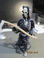 Full body view of Grim Reaper figure holding scythe with black cloak and skeletal body.