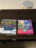 Two 1000-piece jigsaw puzzles side-by-side on a table, one is Sure-Lox Hometown Collection and the other is Night & Day Buffalo.