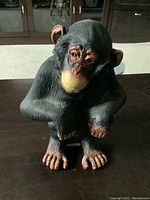 Front view of animatronic chimpanzee showing detailed facial features, hands, and feet, positioned sitting on a table.