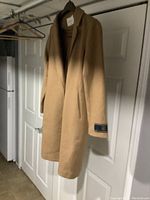Full front view of camel Babaton wool coat hanging on rack