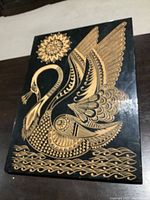 Full view of the rectangular wood engraving showing the swan, sun, and water motif in natural wood color on black background.