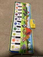 Full view of the children's musical piano play mat on carpet, showing 12 piano keys with animal illustrations and number/star markings.