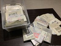 Clear plastic container filled with multiple glassine envelopes containing stamps, visible stamps showing assorted designs and colors.