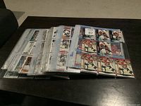 Overview of multiple binders filled with hockey cards in plastic sleeves laid flat on a table.