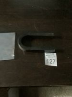 Top-down photo of a large black U-shaped magnet placed on a dark surface with a white label numbered 127 beside it.