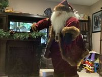 Santa figurine standing beside and leaning on the fireplace decoration with visible greenery on top.