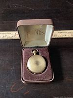 Closed gold-tone Finnex pocket watch resting in original brown velvet-lined case with satin lid interior.