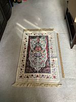 Full view of the Royal Dai prayer mat laid flat on a beige carpet showing the entire mat with fringed edges and a wooden ruler for scale.
