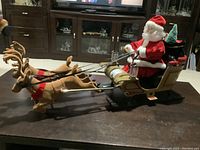 Santa figurine seated in a decorated sled, showing the overall length and detail of the item on a table in a living room environment.