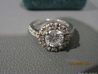 Close-up front view of the silver ring with clear stones on a gray surface, showing main stone and halo.