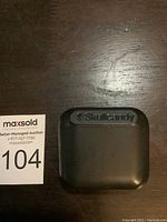 Top view of the black Skullcandy charging case for wireless earbuds on a wooden surface, showing the logo on the lid.