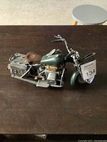 Side view of the Harley Davidson tin motorcycle model showing green body, brown seat, side saddlebags, and mounted holster.