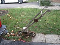 Side view showing the full seeder with long wooden handles, metal wheels, and seed hopper.