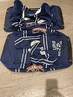 Two navy blue adult hockey gear bags, navy blue with white stripes and orange Islanders branding, lying flat on wooden floor.