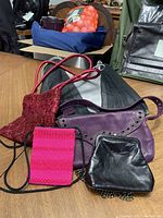 Image showing five assorted fashion bags in different colors and materials, placed on a wooden table with additional items in the background.