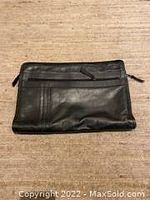 Black leather portfolio laid flat showing front side with outer zippered pocket and smooth leather finish.