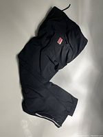 Black Canari cyclewear bike pants folded showing logo patch, elastic waistband and ankle zipper.