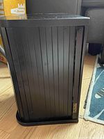 Photo of the closed black vertical CD case on a wooden floor, showing tambour style door and a brass nameplate.