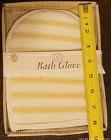 Top view of the exfoliating bath glove folded inside a box with measuring tape showing approx 7 inches length