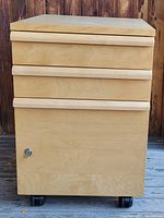 Full front view of the light-colored three-drawer filing cabinet on caster wheels showing the lock at bottom left corner.