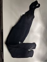 Full view of black Izumi bike bib pants laid out flat, showing length and shoulder straps.