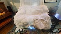 Folded white king size down duvet displayed on a glass table, showing its fluffy and soft texture