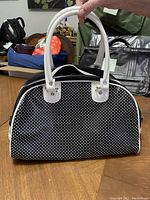 Front view of a black vinyl tote bag with white small polka dots and white handles, showing the overall shape and condition.