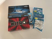 Photo showing boxes of Nitro Blaster, Ram Tour Titanium, and Maxfly Noodle Ice golf balls along with two packages of white golf tees.