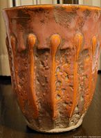 Close-up side view of the textured orange ceramic vase showing raised vertical drip style decorations on the outer surface.