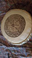 Round beige pillow with central beaded embroidery and ruched border on a patterned fabric background.