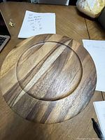 Photo showing one wooden charger plate with natural wood grain, 12.75 inches in diameter, placed on a wooden table with measuring notes visible.