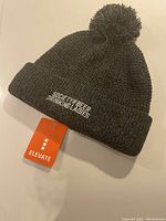 Dark gray knitted toque with pom-pom, showing embroidered text 'Society of Beer Drinking Ladies' and attached original Elevate brand tag.