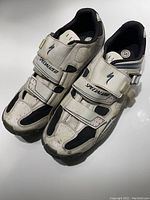 Photo showing a pair of used Specialized cycling shoes, white with black and gray accents, two strap closures and a buckle, with size label 45 visible.