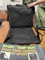 Photo of unfolded black folding camp seat showing seat and backrest with adjustable straps and carrying handle.