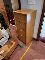 Front view of a small pressed wood chest with five drawers and rounded knobs. Light wood finish, placed on a carpeted floor.