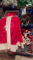 Photo showing a red and white Santa jacket along with Christmas ornaments and decorations in bins and crates.