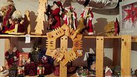 Photo showing assorted Christmas Santas, fabric figurines, wooden wreath, village decorations, and tall wooden stands on display shelving