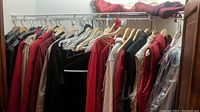 View of outerwear coats and vests on hangers in a closet showing red, black, beige garments.