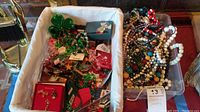 Basket containing holiday-themed costume jewelry, including shamrock pins, packaged holiday pins, and various earrings and bracelets.