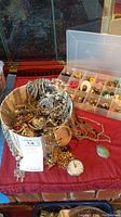 Wide view of mixed costume jewelry including tangled chains, pocket watch, and earring storage box with multiple sections.