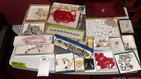 Photo showing assorted costume jewelry pieces including silver-tone chains, red and white bead strands, and various earrings in boxes.