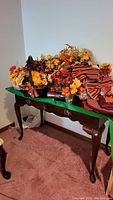 Wooden desk with two drawers, brass tone pulls, and some decorative autumn floral arrangements on top