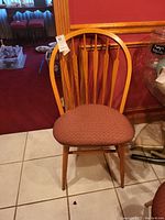 Front view of one wooden bow back dining chair with reddish patterned cushioned seat on tiled floor.