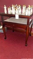 Full front angled view of wooden display table with lift-top glass cover and drawer, shown with figurines on top.