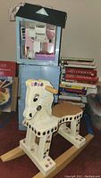 Photo showing the rocking horse in front of a blue dollhouse and a stack of cookbooks.