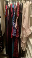 Photo of several women's dresses and tops hanging tightly on hangers in a closet. Colors include leopard print, black, red, blue, and white. Variety of fabrics and styles visible.