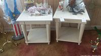 Pair of white square wooden end tables placed side by side on carpeted floor with some items on top and scratching visible.
